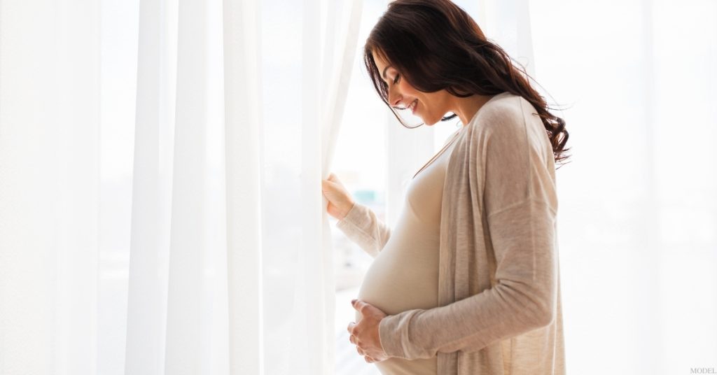 Pregnant woman standing in front of white curtains (model)