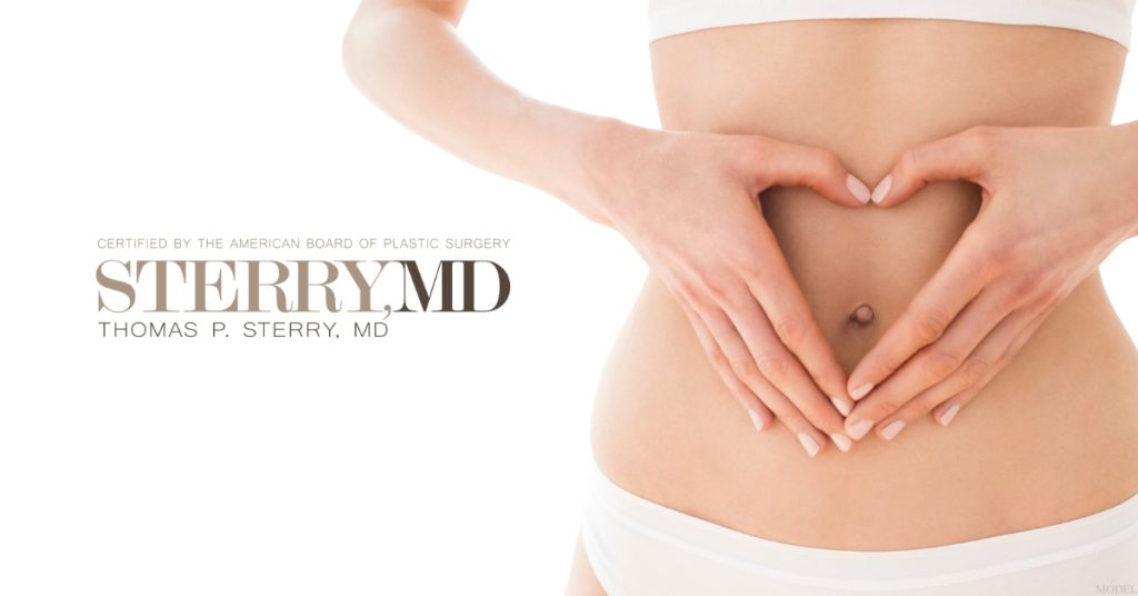 A woman is holding her stomach and making a heart shape with her hands (model)