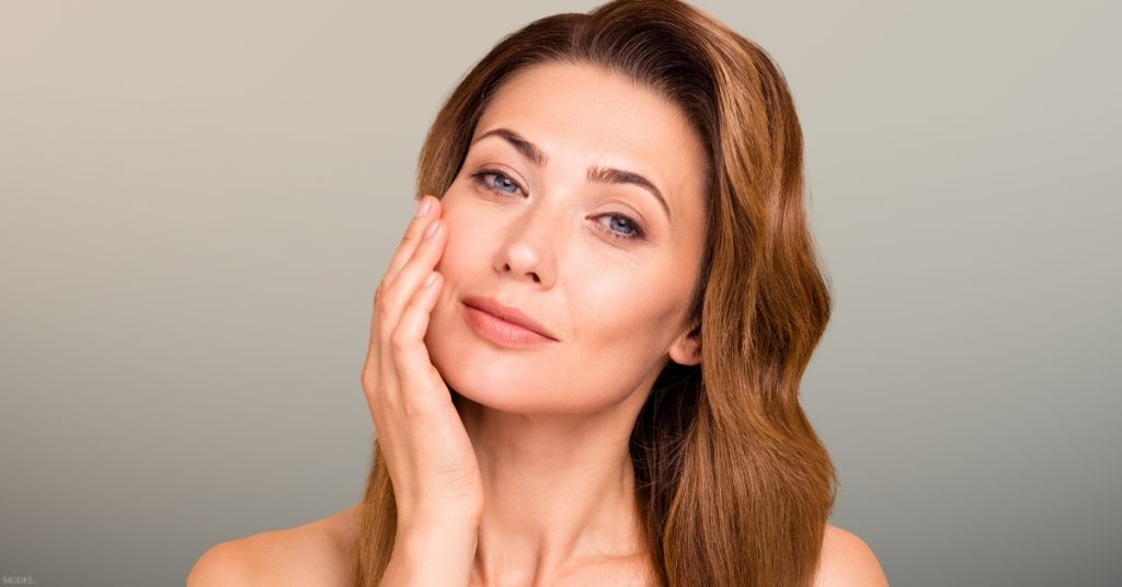 Woman with long brown hair touching their face (model)