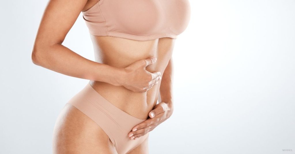 A woman in a tan undergarment holding their stomach. (Model)